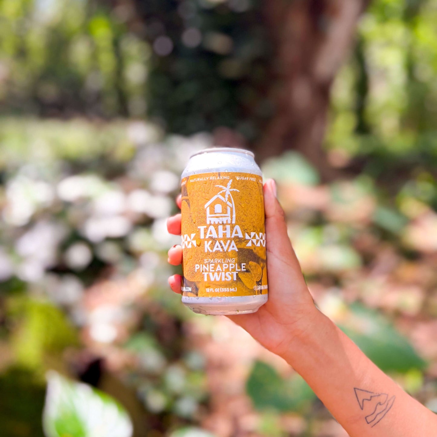 Hand holding Taha Pineapple kava can in tropical foliage